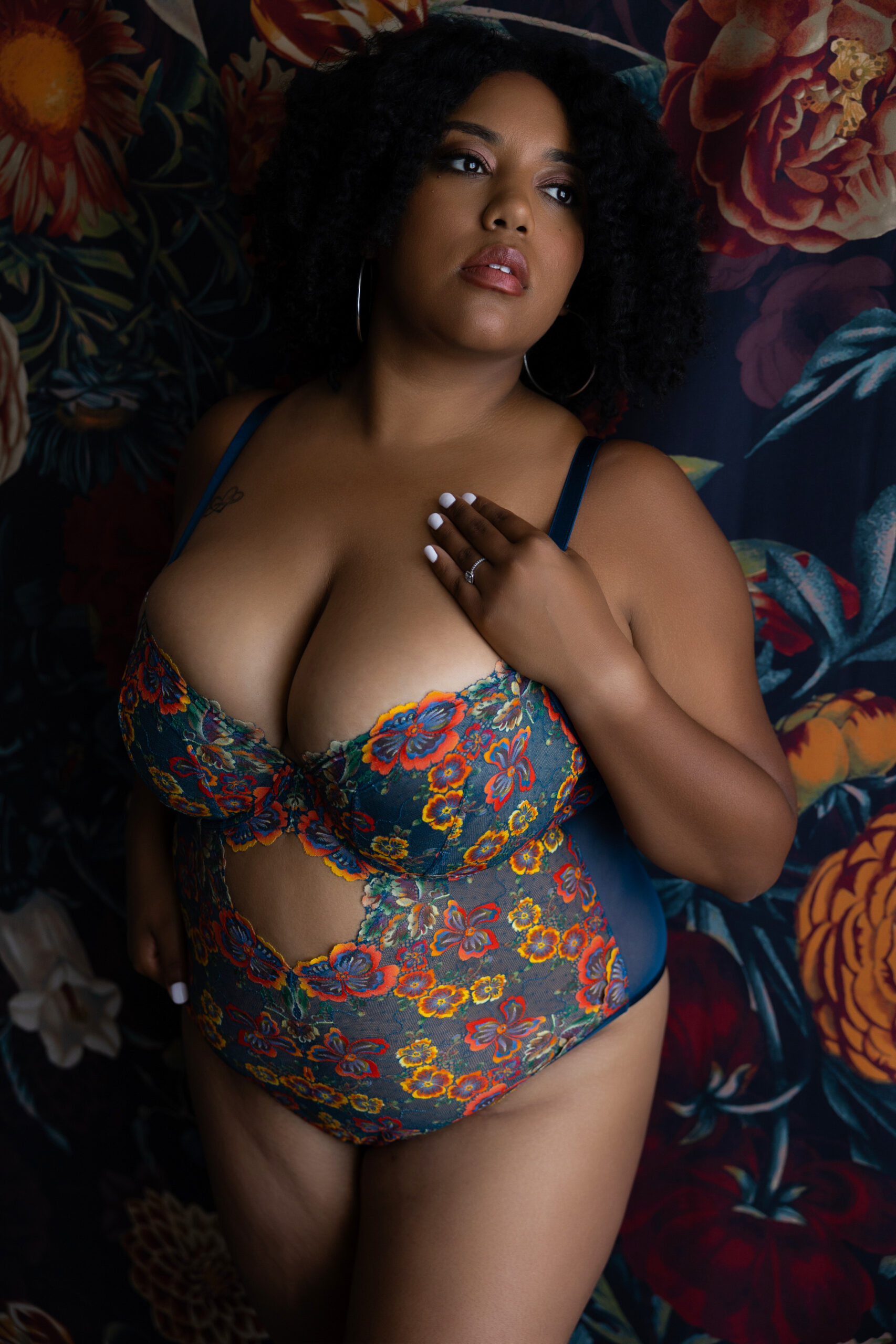 A woman stands against a flower mural that matches her flower print lingerie while gazing out a window with a hand on her chest after enjoying day spas in baltimore