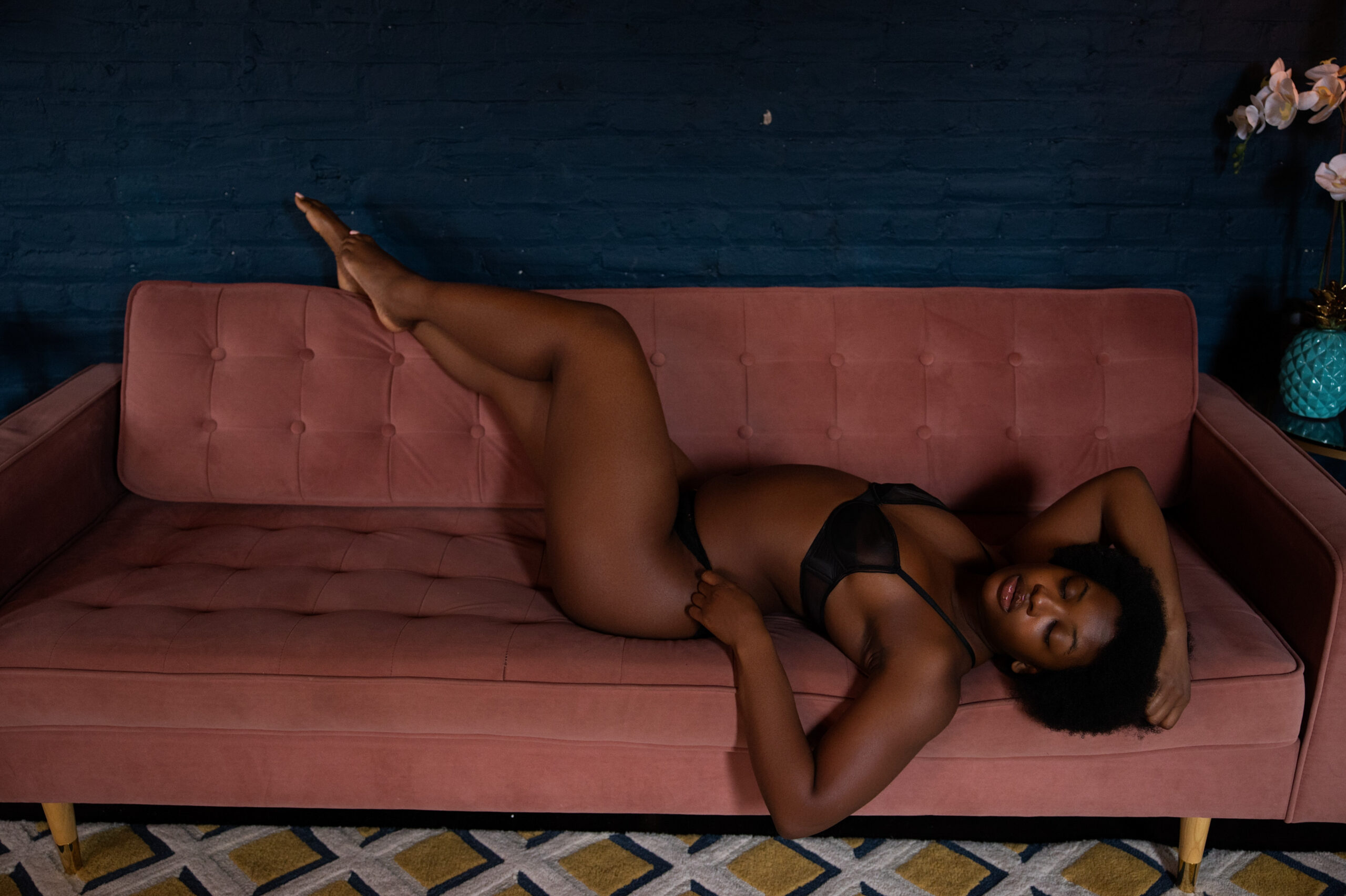 a woman relaxes across a pink couch with a hand in her hair and feet up on the back