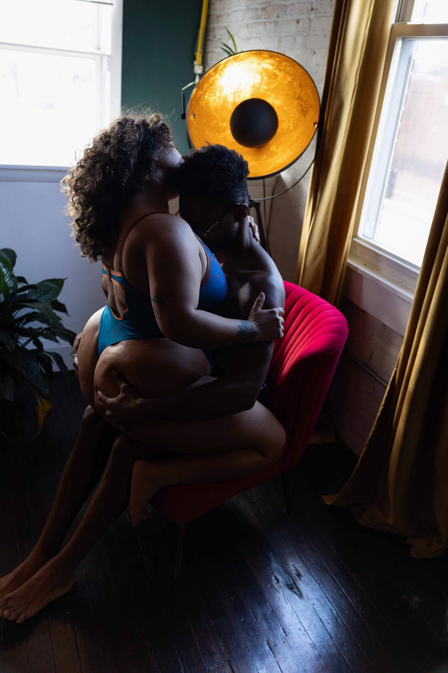 A woman in blue lingerie sits in the lap of partner as they embrace in a red chair in a studio after some marriage counseling in northern virginia
