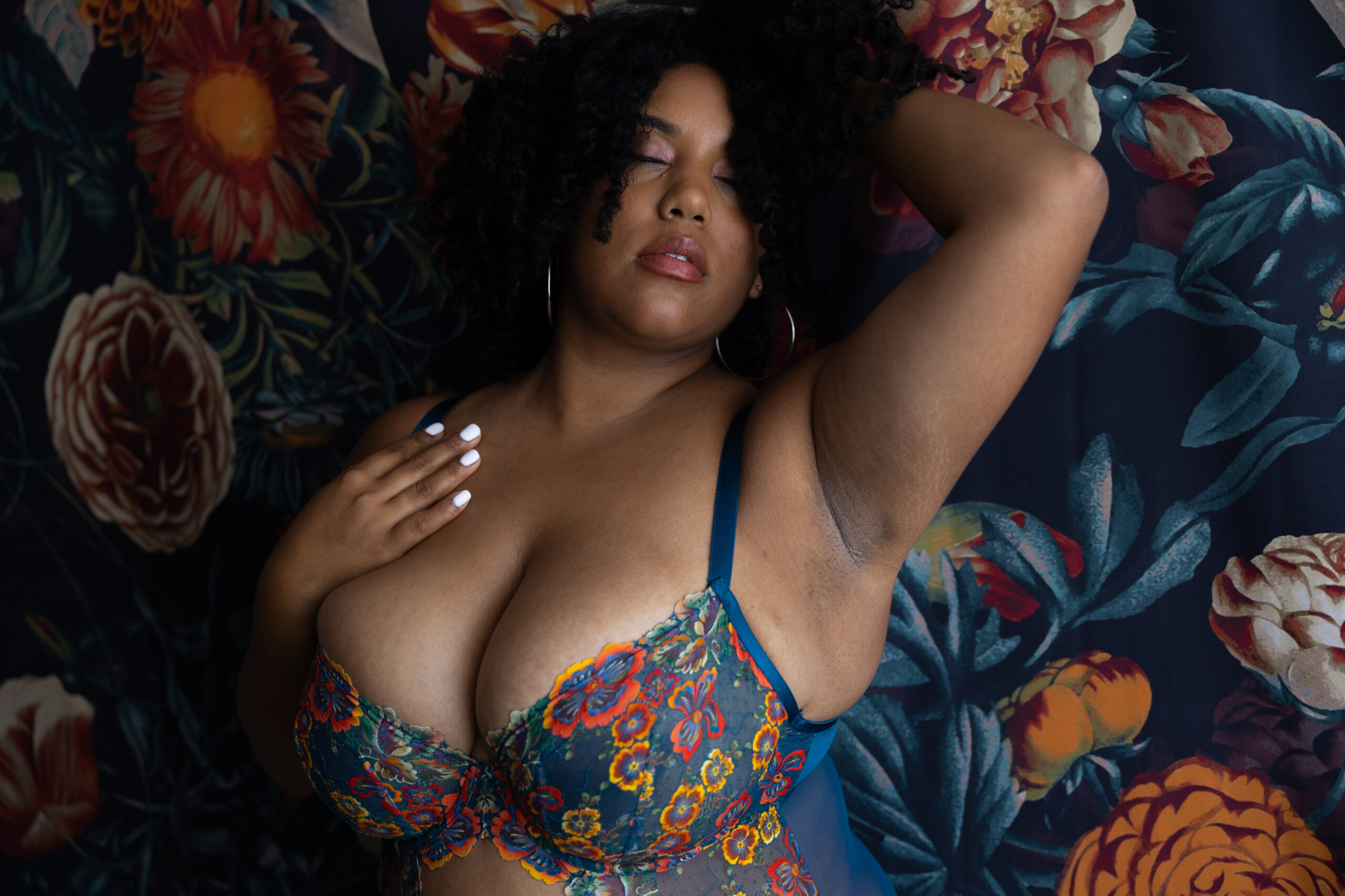 A woman in flower print lingerie lays on a matching bed with a hand in her hair and one on her chest after some pole fitness in northern va