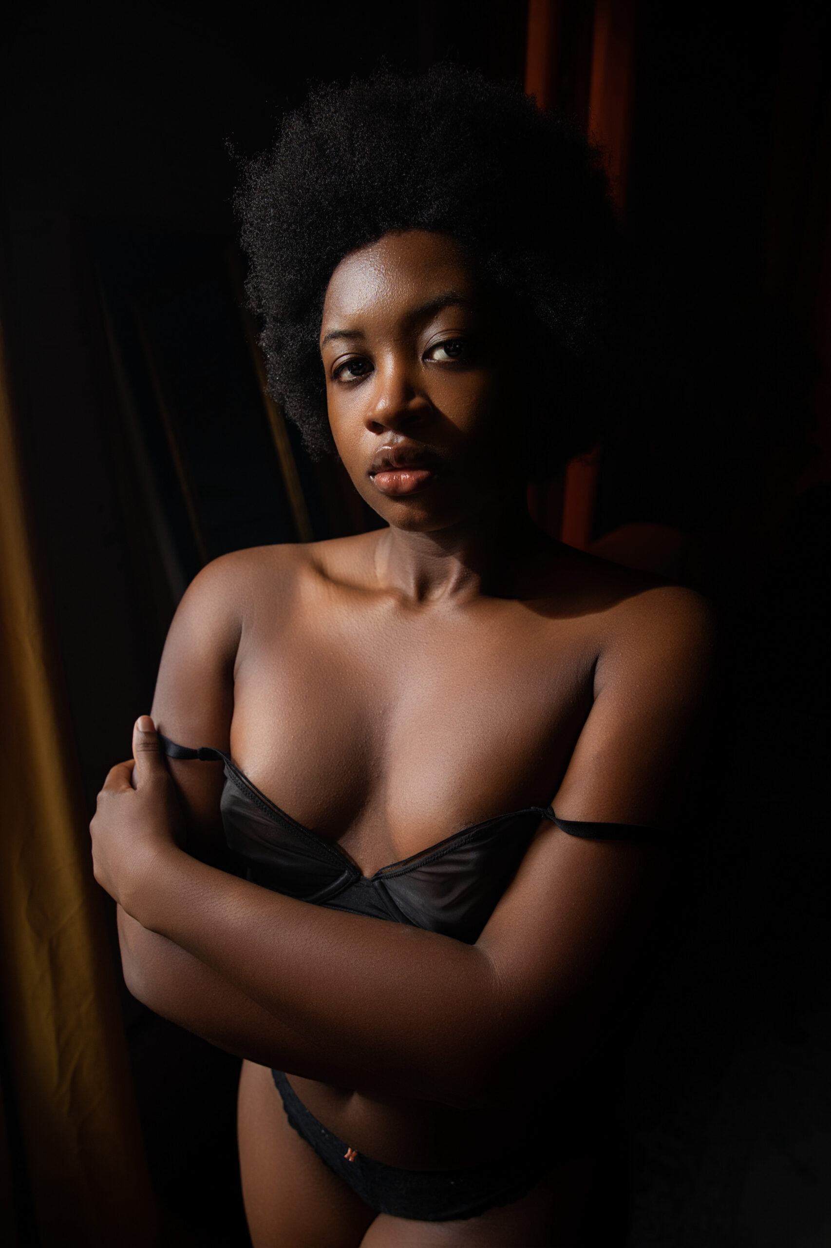 A woman with arms crossed stands in a studio with her black bra straps falling off her shoulders after enjoying romantic restaurants in baltimore