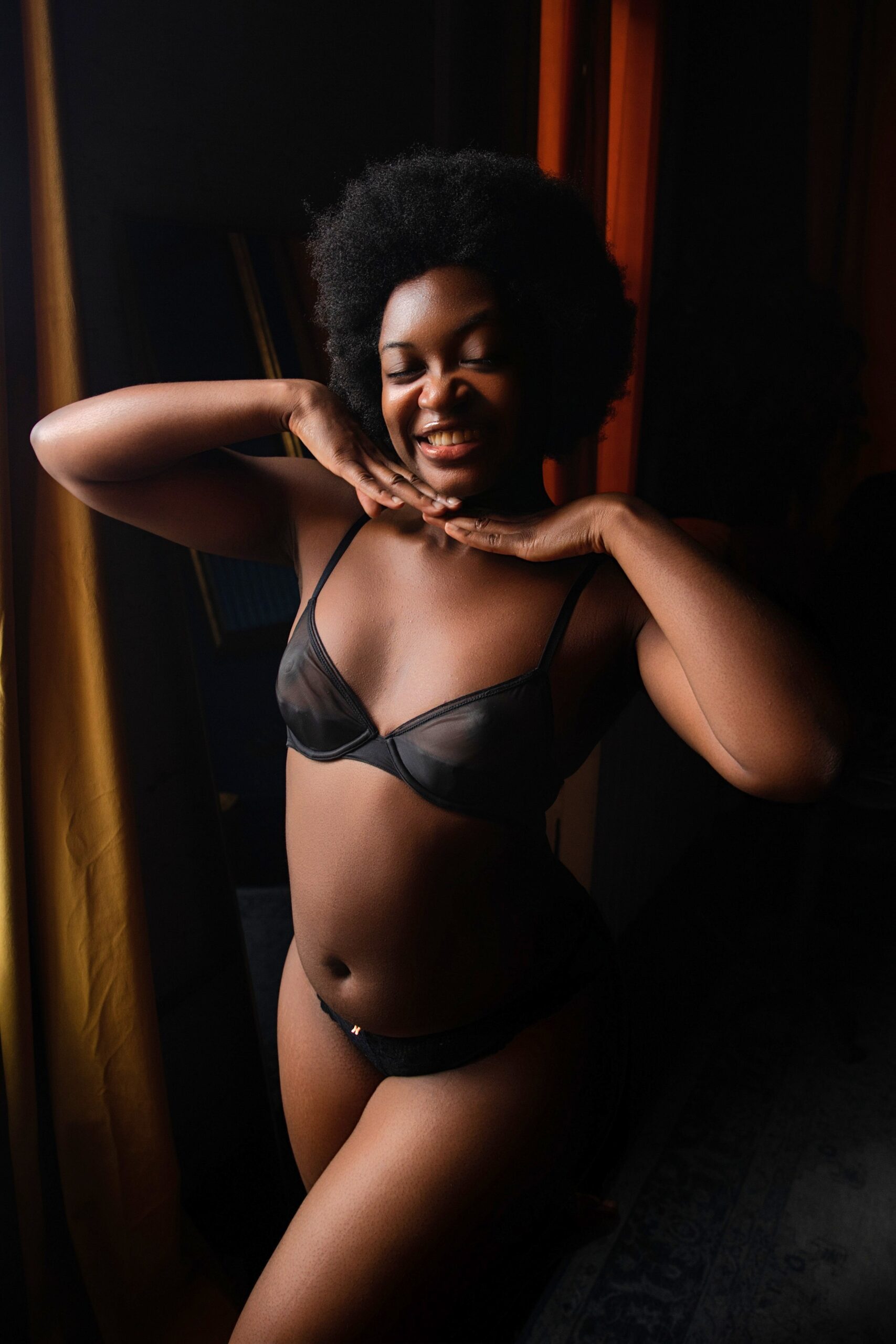 A woman smiles with hands under her chin while standing in black underwear after getting waxing in baltimore