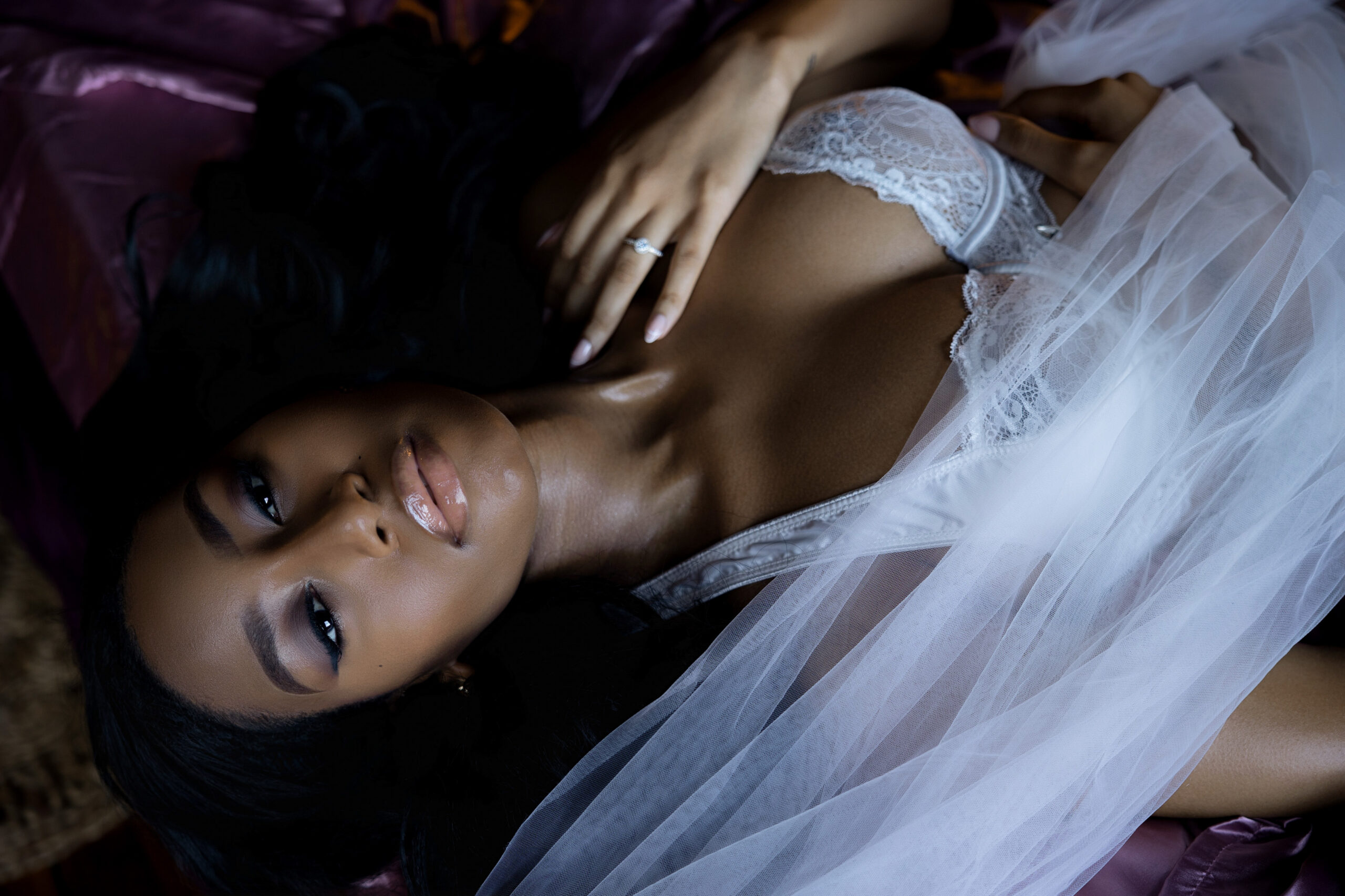 A woman lays on a bed with her veil draped across her in white lace bra from bridal shops in northern va