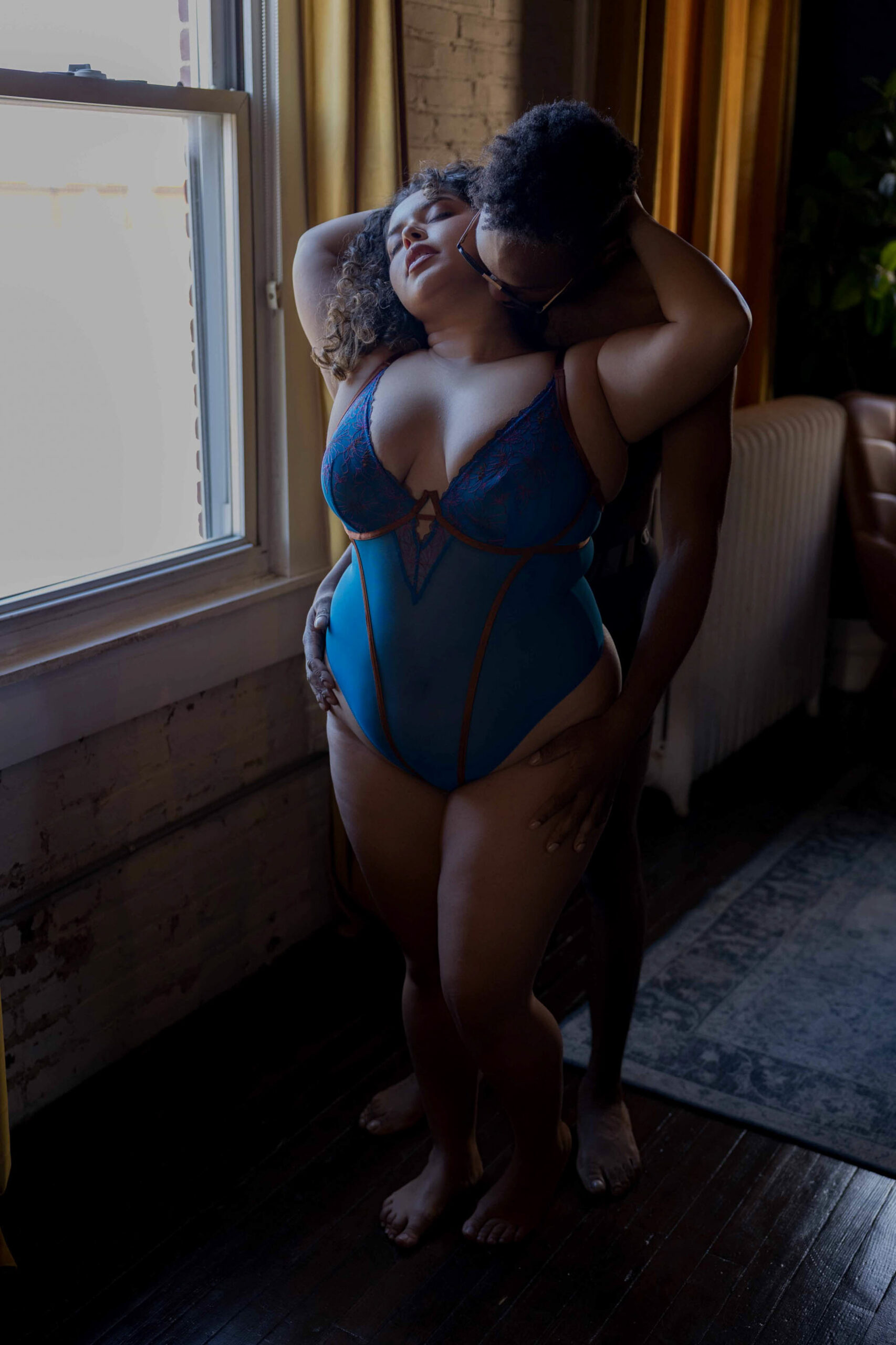 A woman wearing blue lingerie is kissed and held by a man from behind while standing in a window at one of the luxury hotels in northern virginia