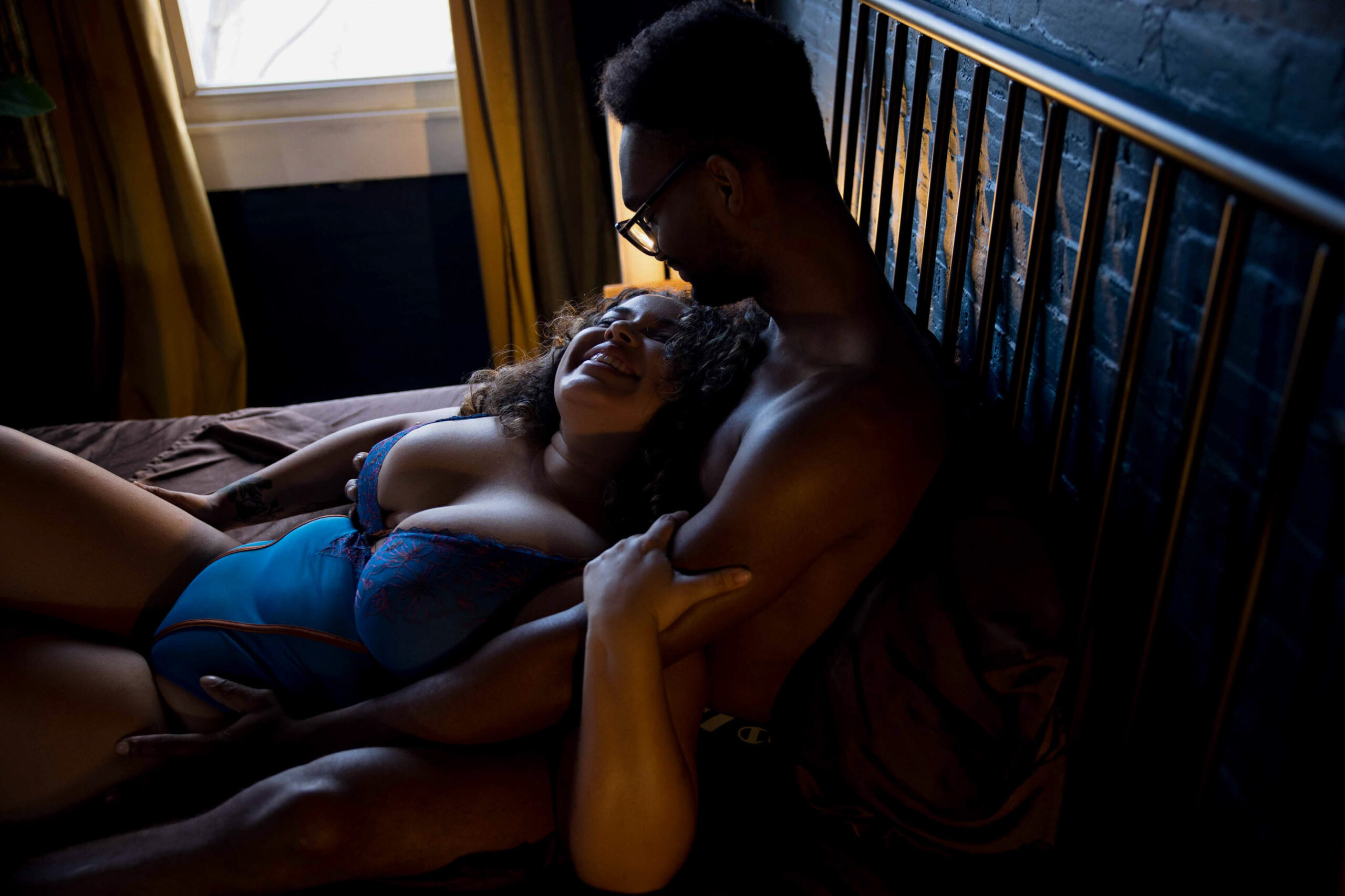 A woman in blue lingerie lays in the lap of her man on a bed as they smile at each other after staying at luxury hotels in northern virginia