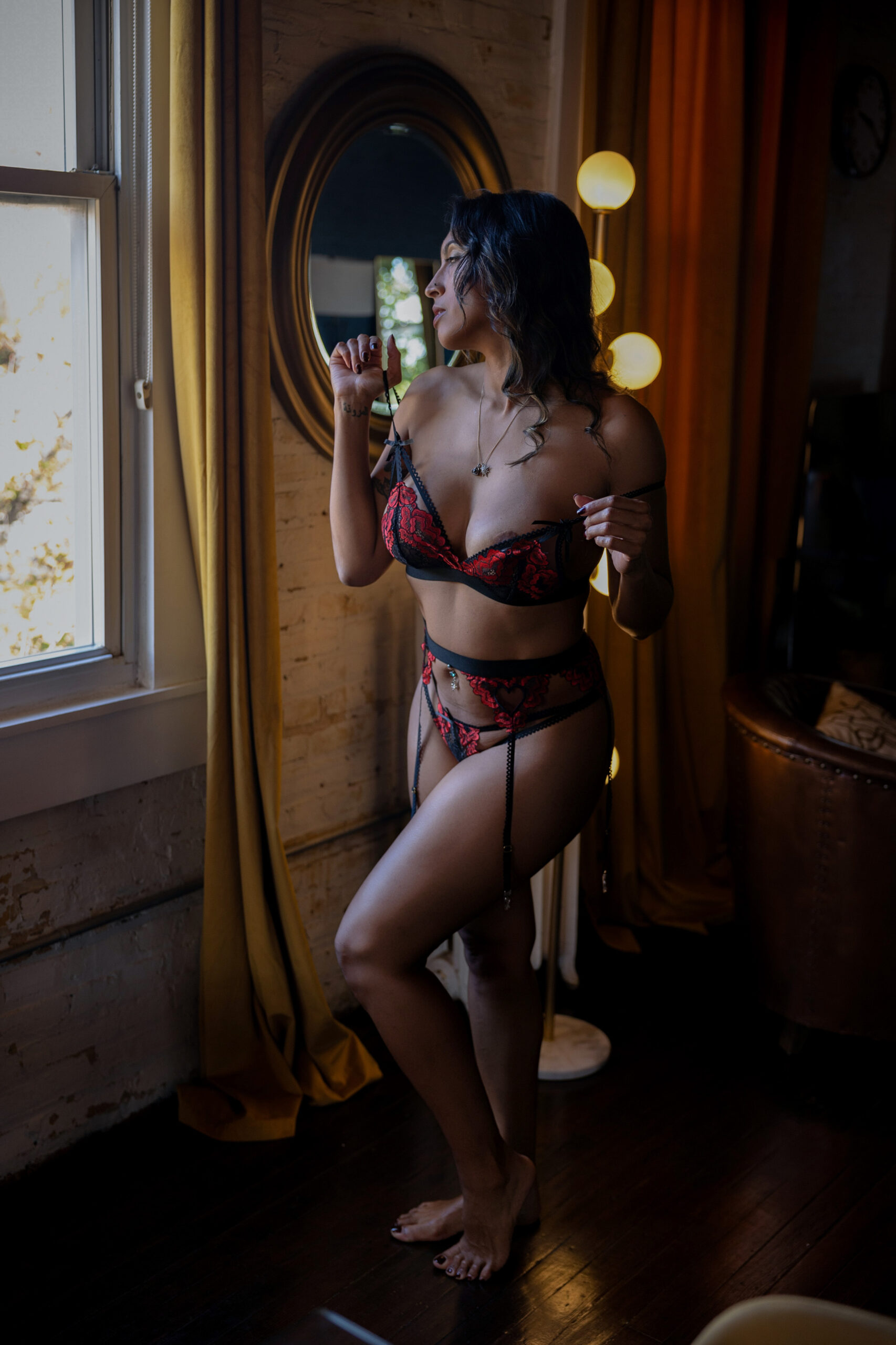 A woman stands in a window in black and red lace lingerie pulling on her straps after finding botox in maryland