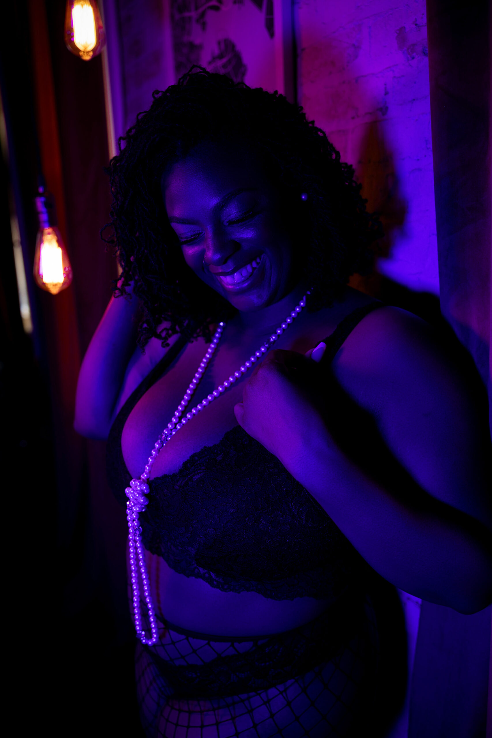 A woman laughs while leaning on a wall in a pearl necklace after some pole fitness in maryland