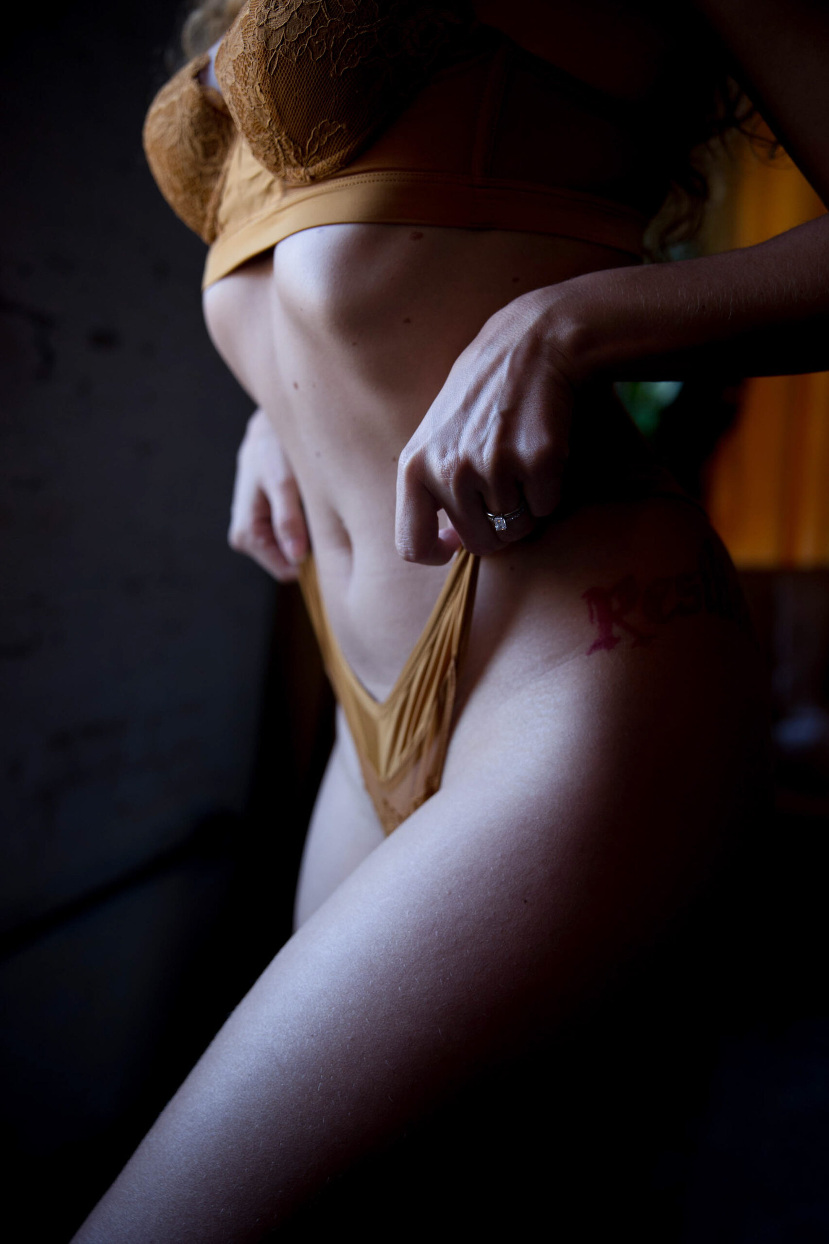 Details of a woman pulling up on the straps of her yellow lingerie in a studio from a la mode intimates