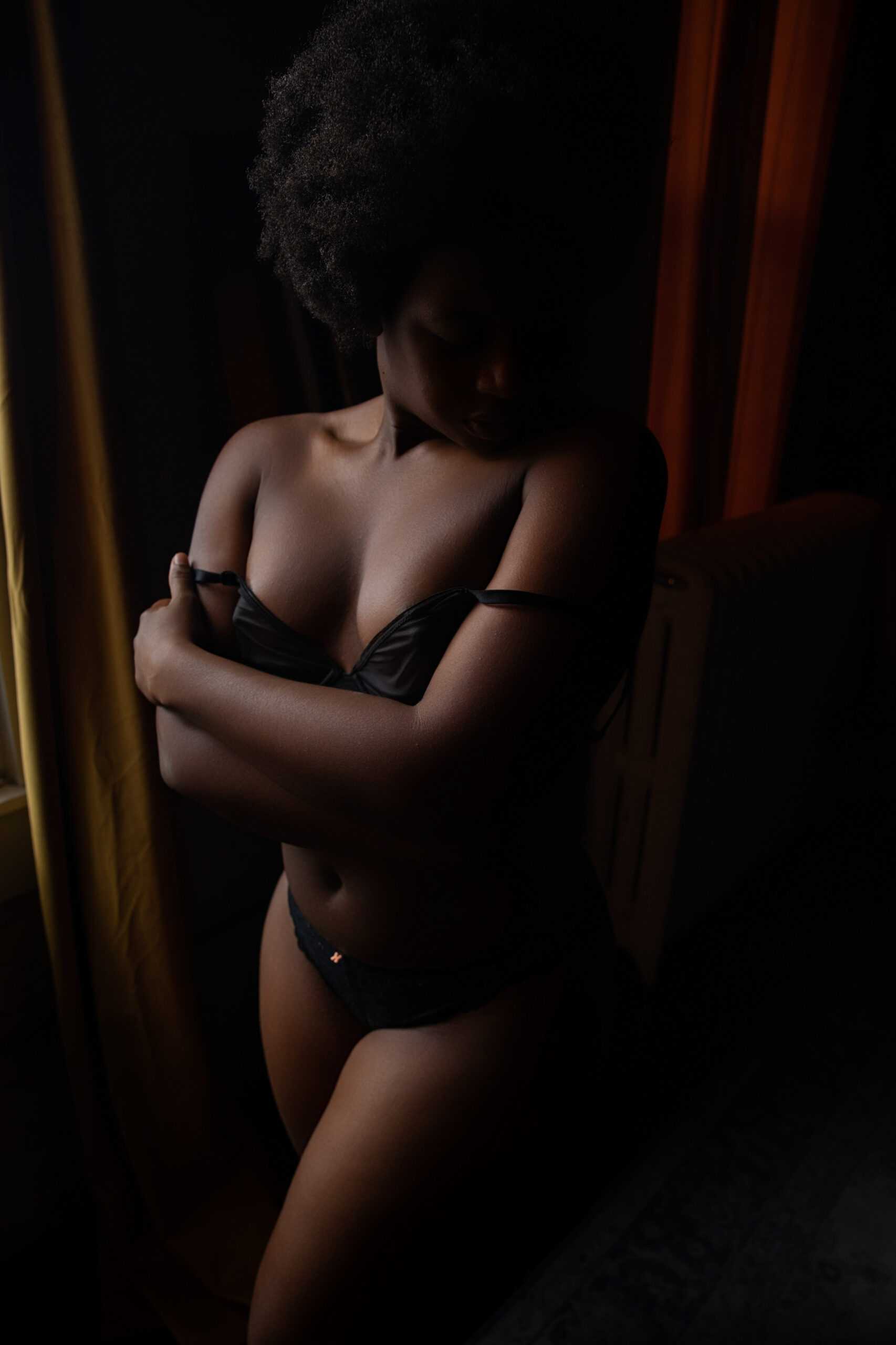 A woman looks over her shoulder while standing in a window with arms crossed covering her black bra from best rack around