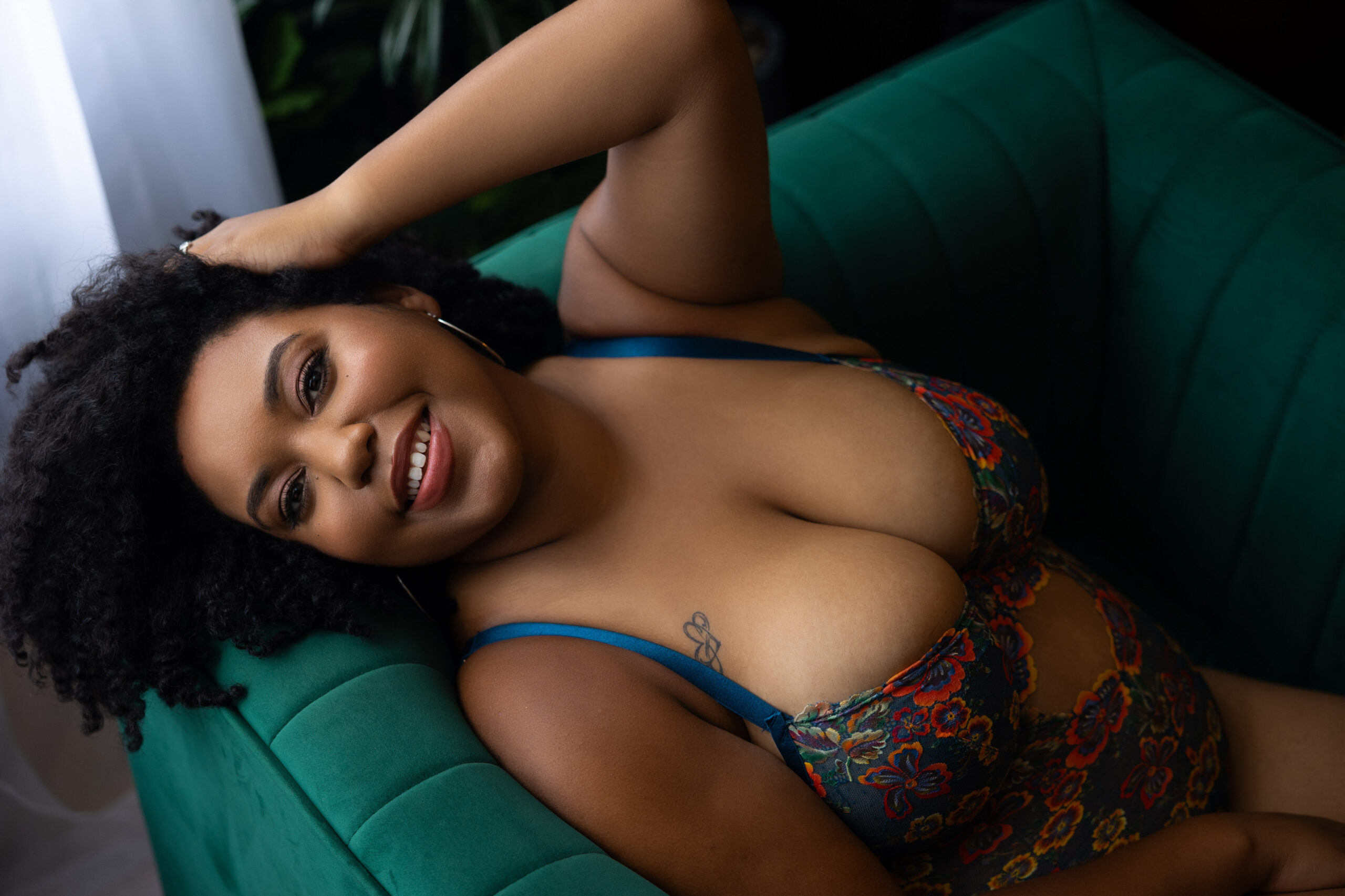 Woman smiling leaning on a green couch during a transformative boudoir session