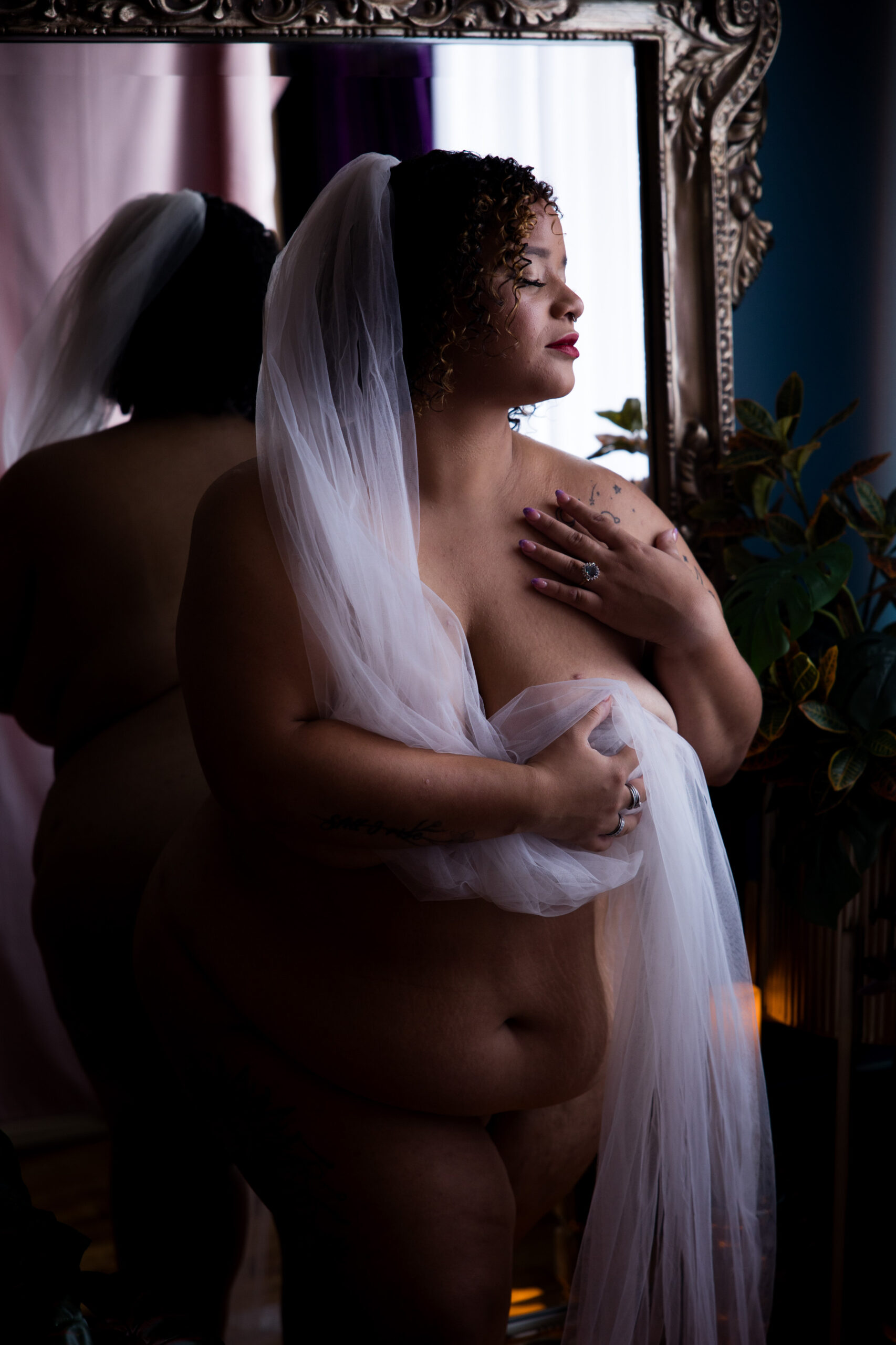 A bride covers her chest with her veil while standing in a mirror