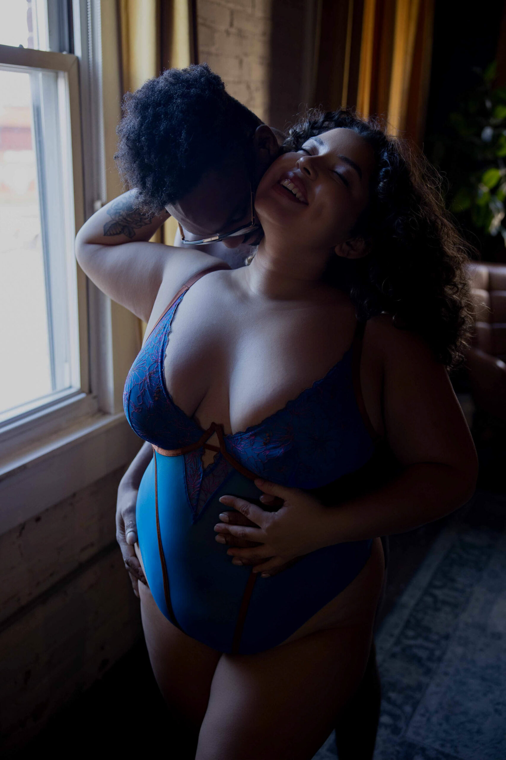 A happy woman embraces her partner while standing in a window in a blue bodysuit during their romantic getaways in maryland